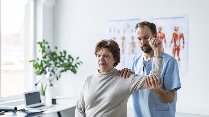 A physical therapist helps a senior woman with her shoulder.