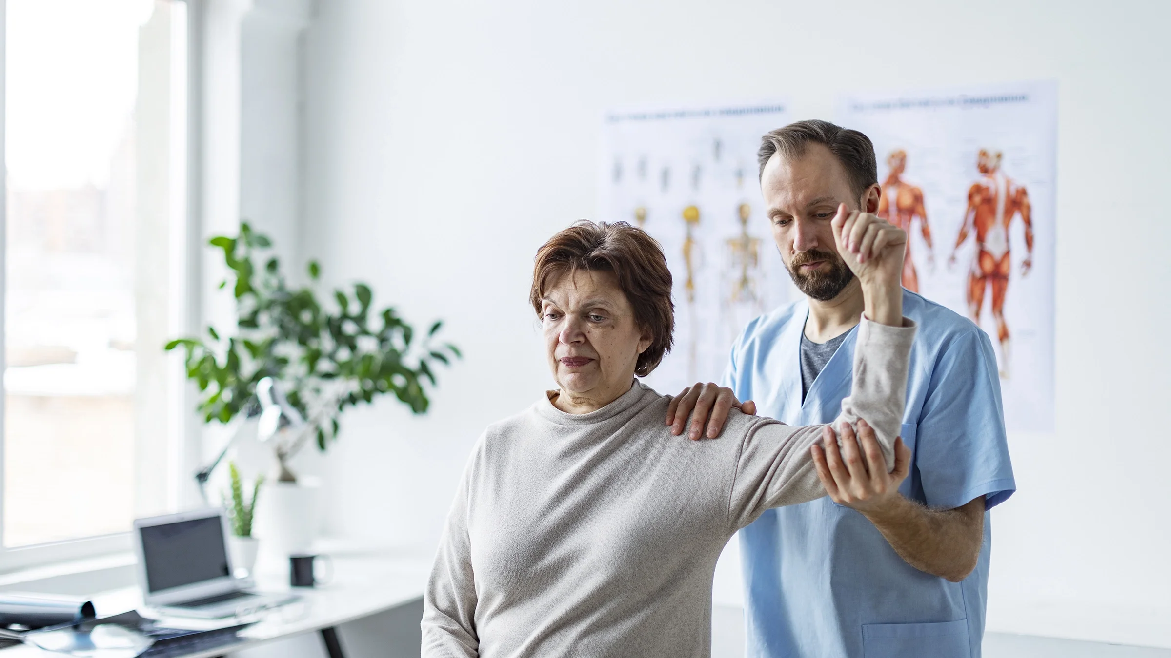 A physical therapist helps a senior woman with her shoulder.