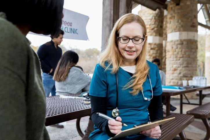 Nurse filling out paperwork on a clipboard for a new patient at an outdoor pop-up free clinic.
SDI Productions/E+ via Getty Images