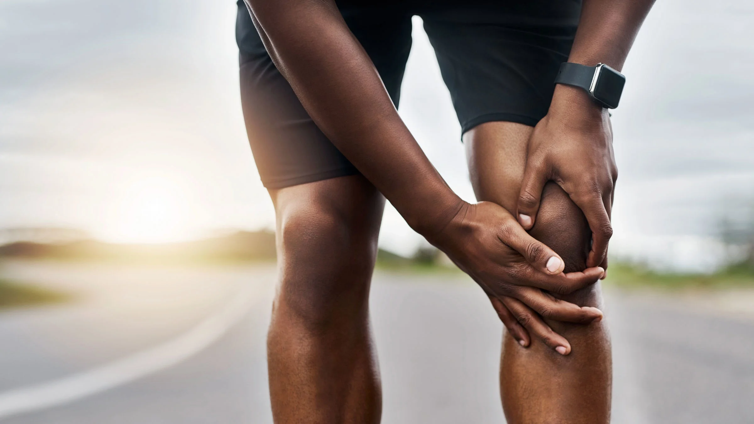 Close-up shot of a man suffering knee pain while exercising outdoors.