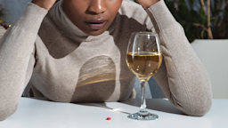 A cropped shot of stressed out person looking at a wine glass and pill on a table. 
Srdjanns74/iStock via Getty Images 