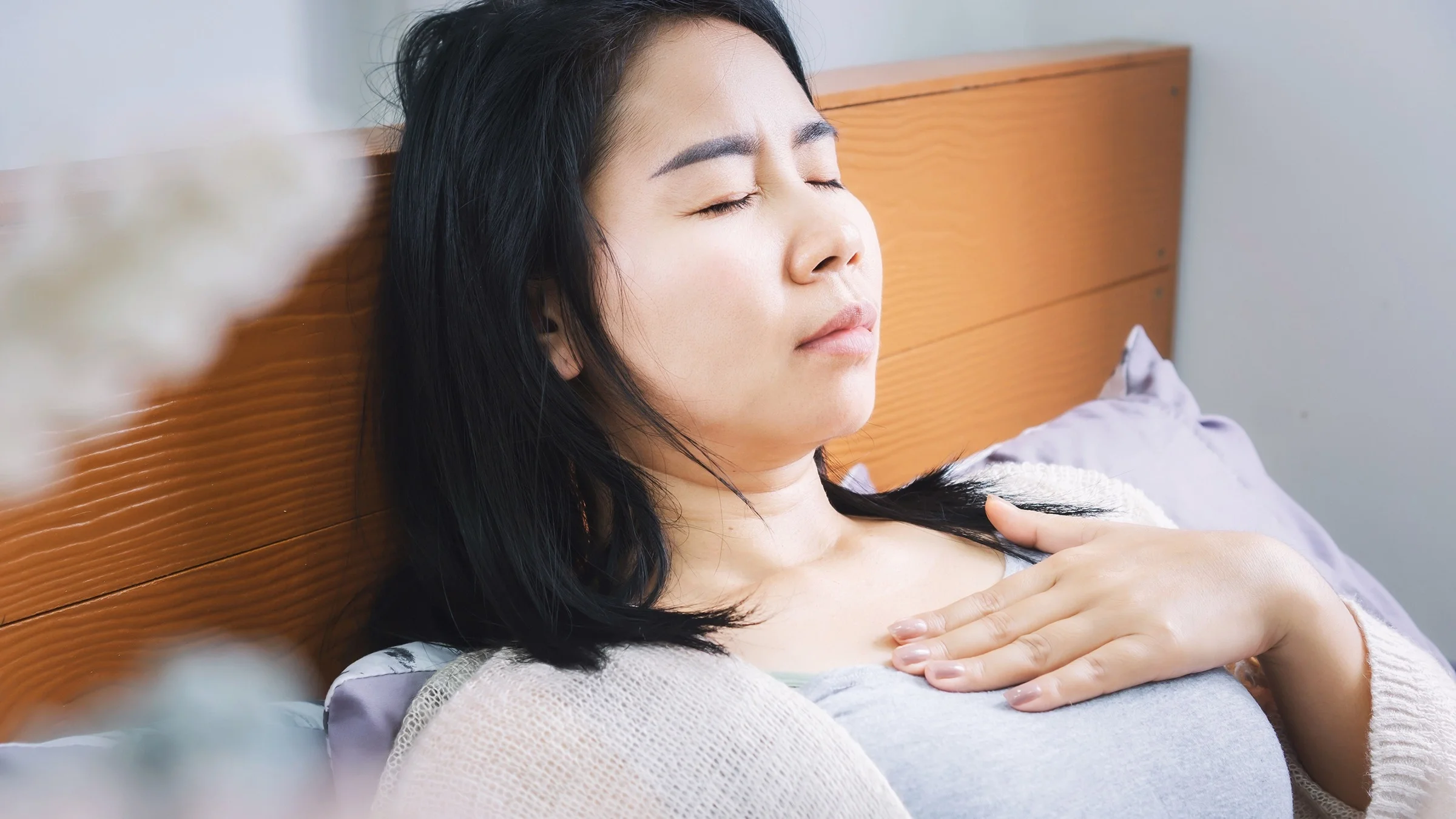 Close-up portrait of a young woman having chest or throat pain. She has her eyes closed and she is laying down in bed.