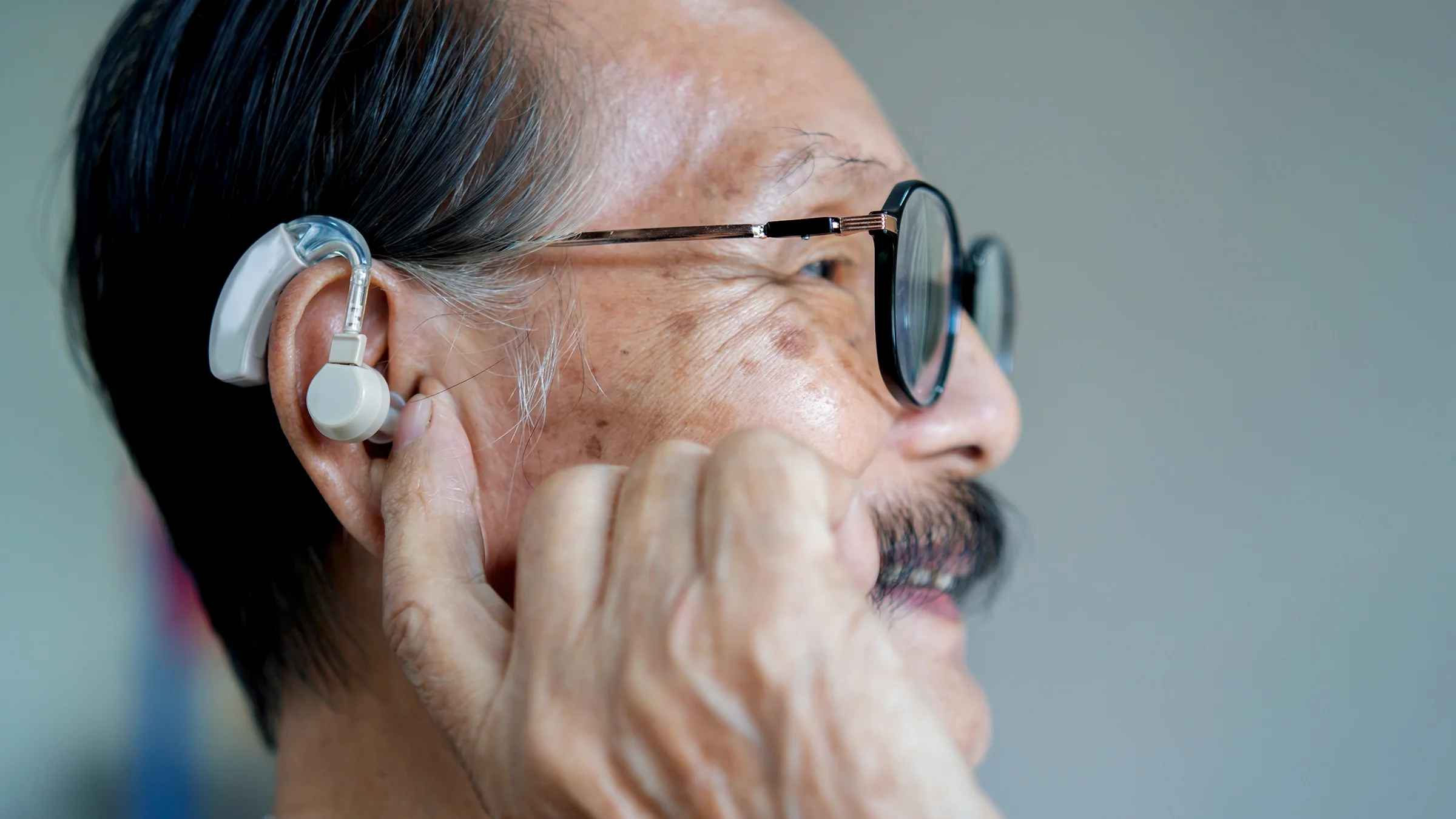 Older man adjusting his hearing aid.