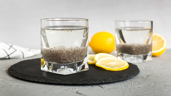 Glasses with chia seeds and water are on a table with slices of lemon. 