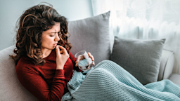 A woman on a couch takes a pill to ease pain.
dragana991/iStock via Getty Images Plus