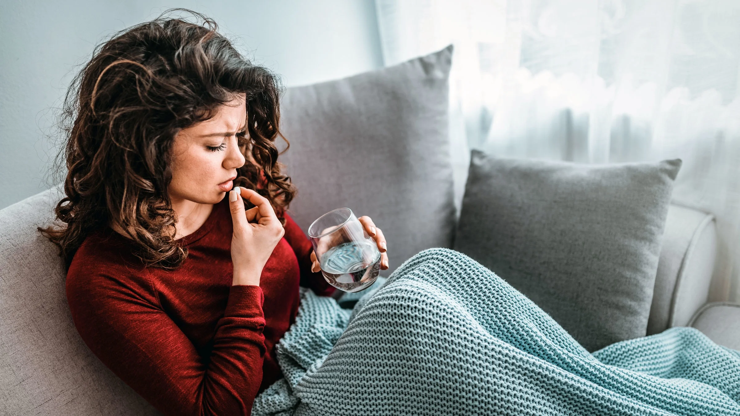 A woman on a couch takes a pill to ease pain.