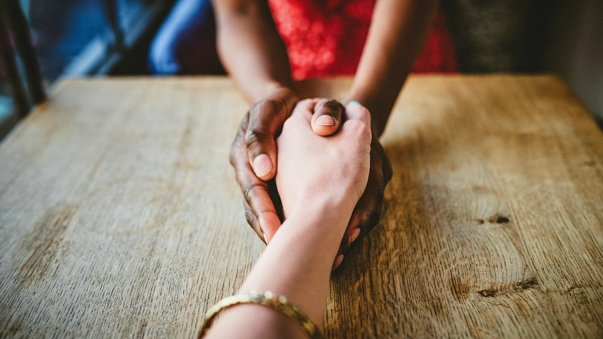 Close-up of two people holding hands across the table.