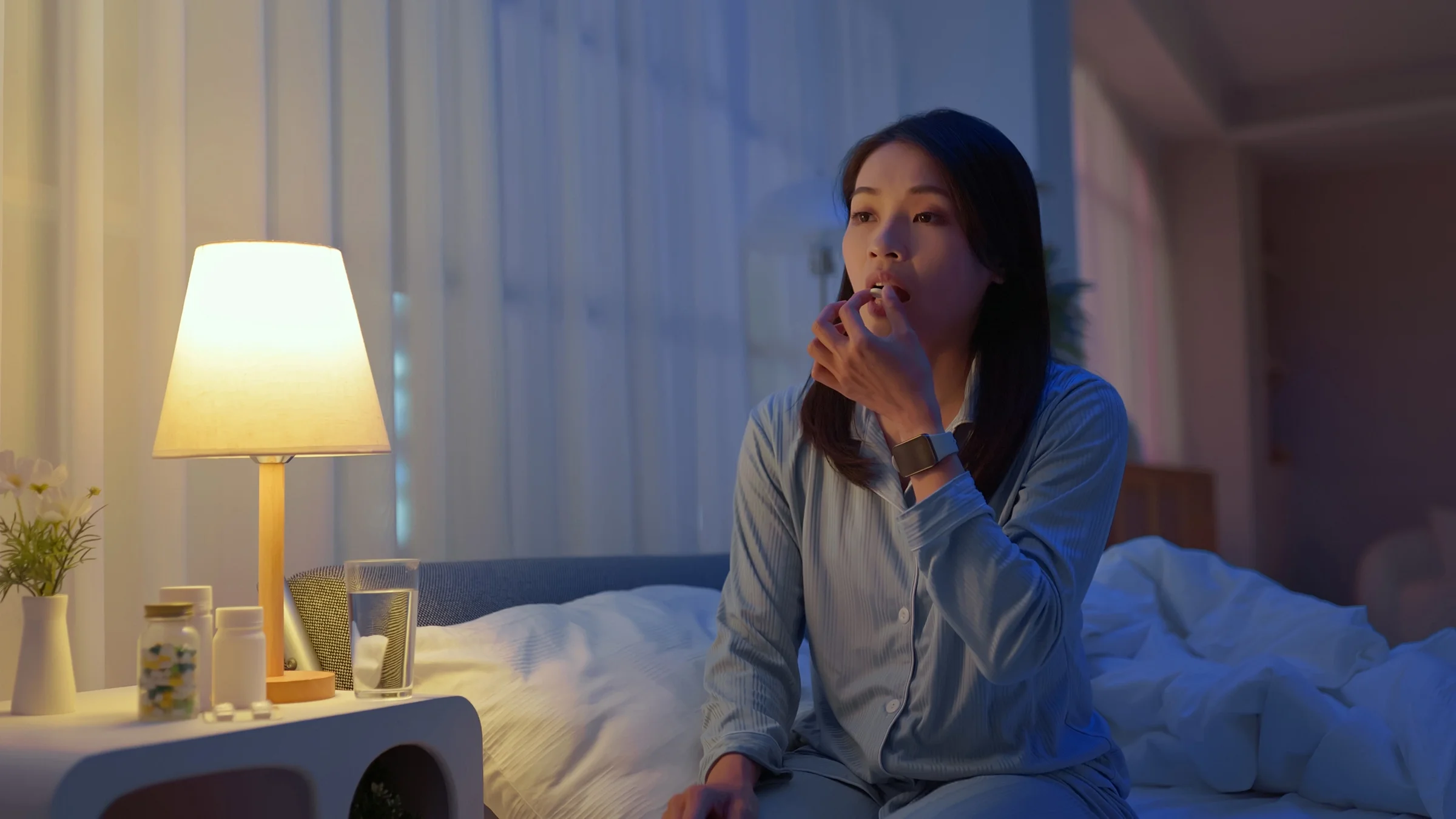 A woman takes her medication while sitting on her bed.