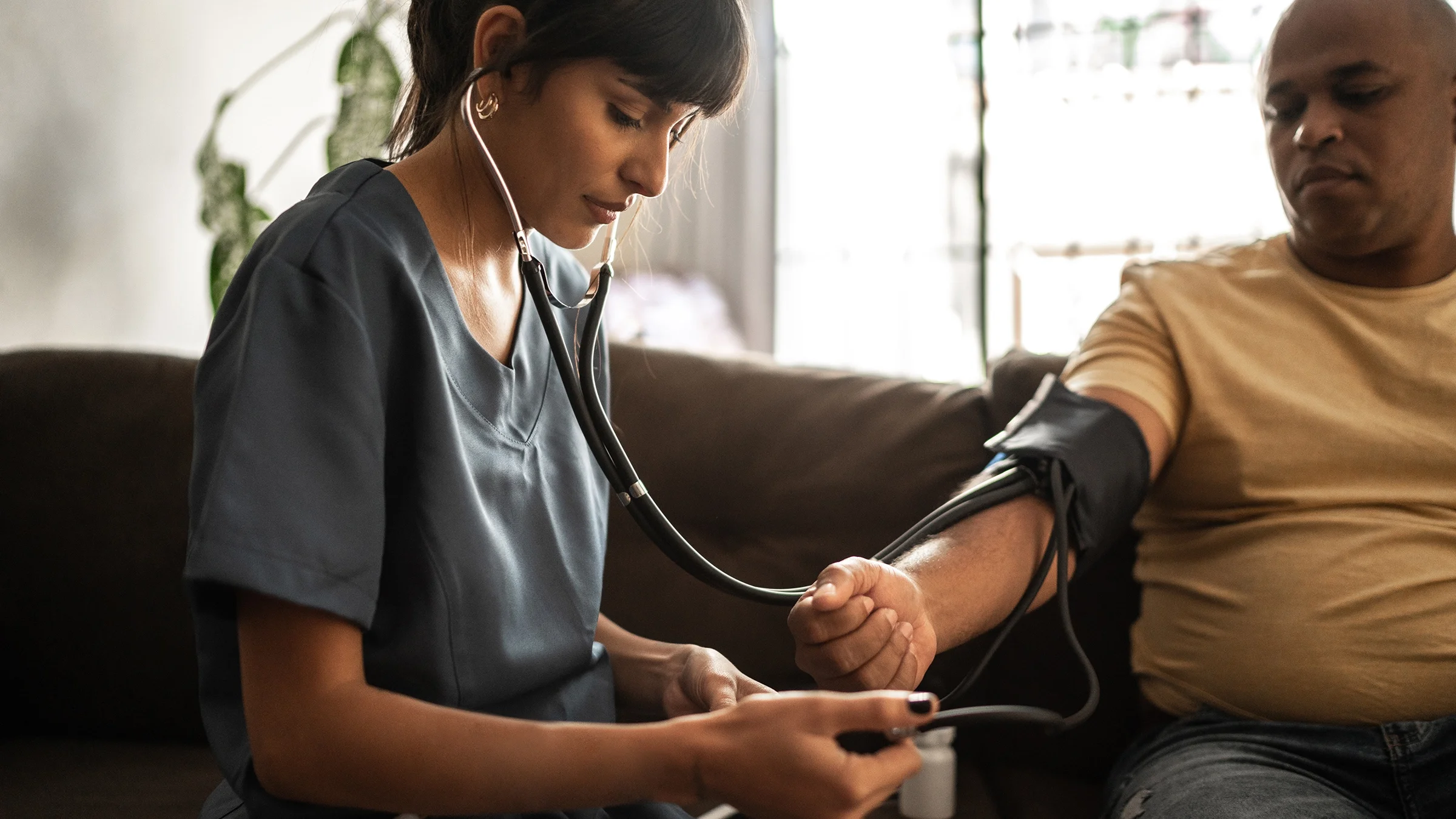 A medical professional checks a patient's blood pressure during a home visit.