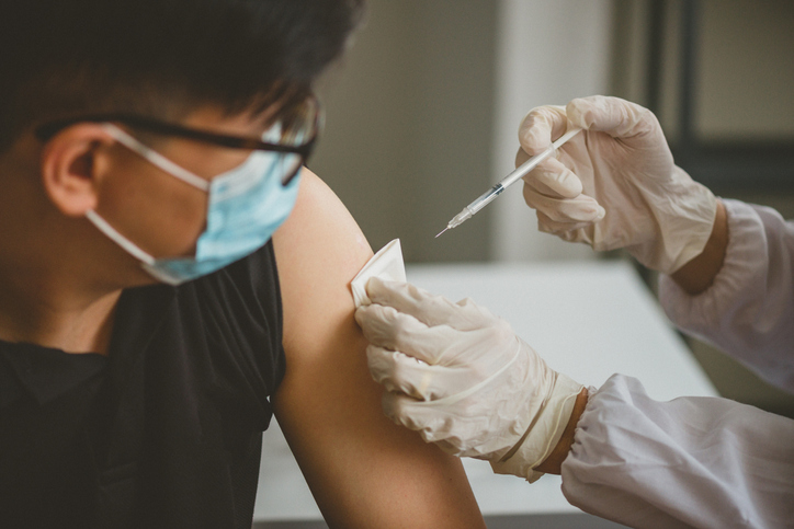 Close-up of a young man getting a vaccine while wearing a blue medical face mask.