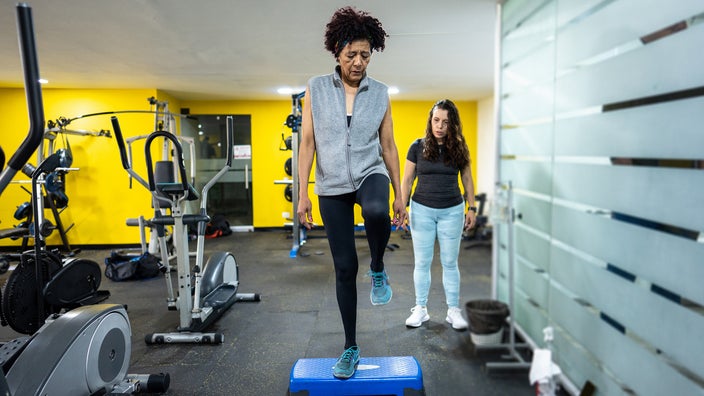 A woman balances her left leg as she stands on a step aerobics equipment in the gym.