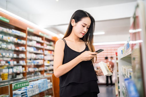 Young woman at a drugstore using her smart phone to scan a barcode on a medicine box.