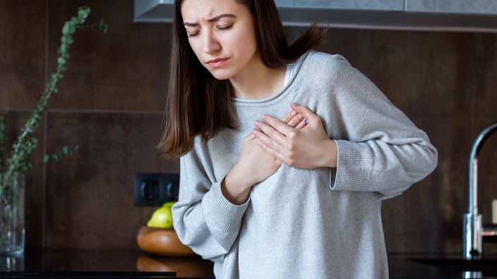 Portrait of a young woman clutching her chest and heart area in pain.