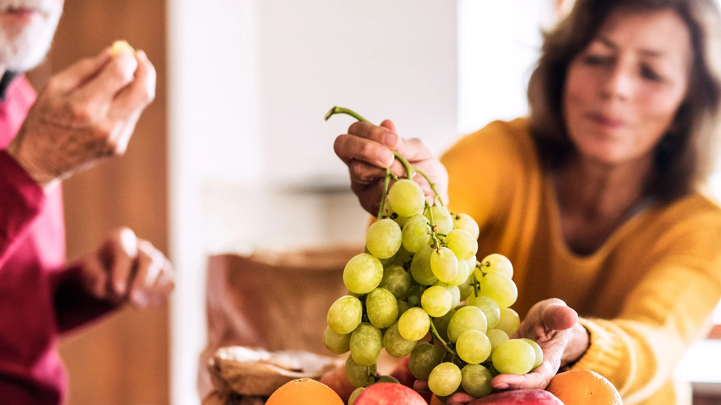 A close-up image shows a woman reaching for a cluster of grapes.