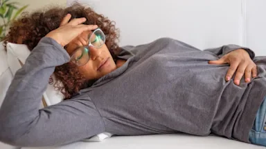 Woman suffering from stomach pain laying on the couch with her hand on her forehead.
tommaso79/iStock via Getty Images