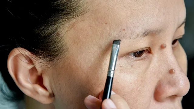 hair-loss: makeup: closeup woman applying makeup to thinning earbrows-689579784