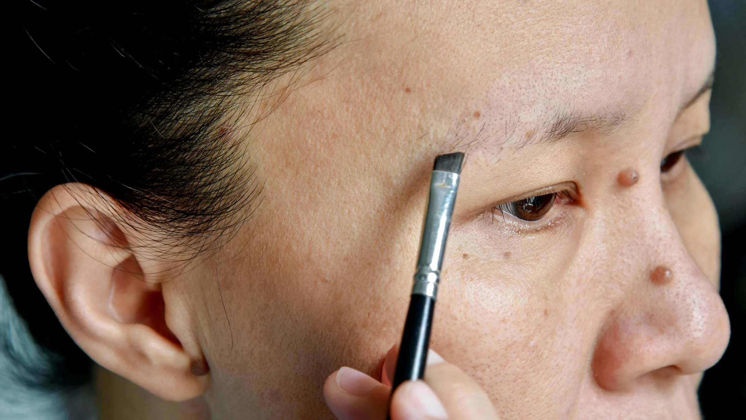 Close-up of a woman putting on makeup to cover her thinning eyebrows.