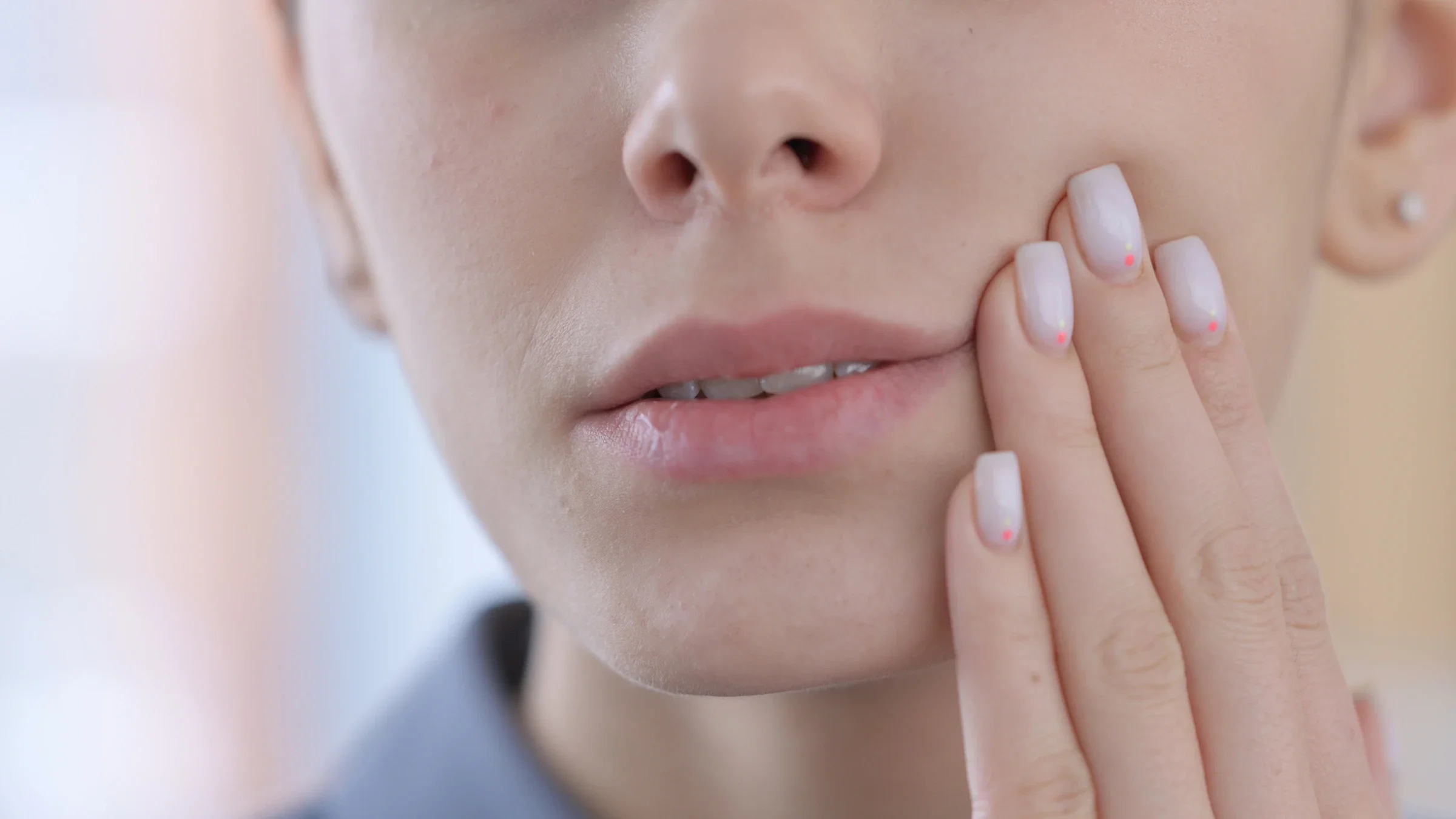 Close-up cropped image of a woman rubbing her cheek because of tooth pain. She has light pink painted nails.
Zmaster/iStock via Getty Images
