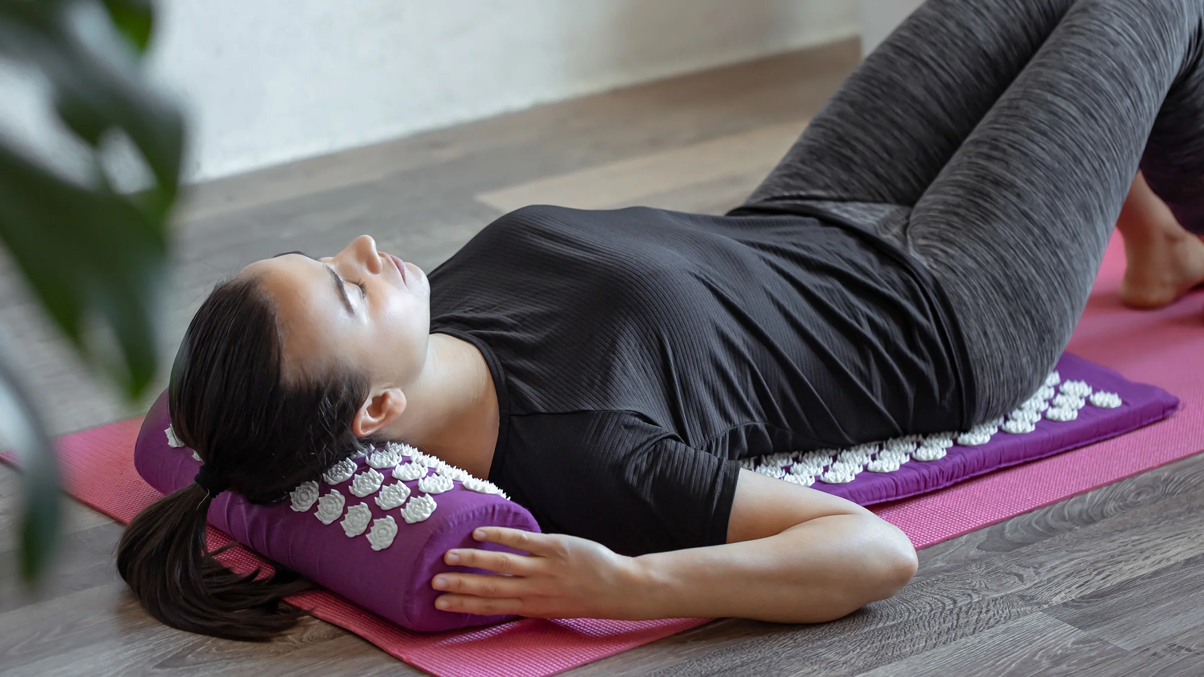 A woman lies on a purple acupuncture massage pillow and a mat.