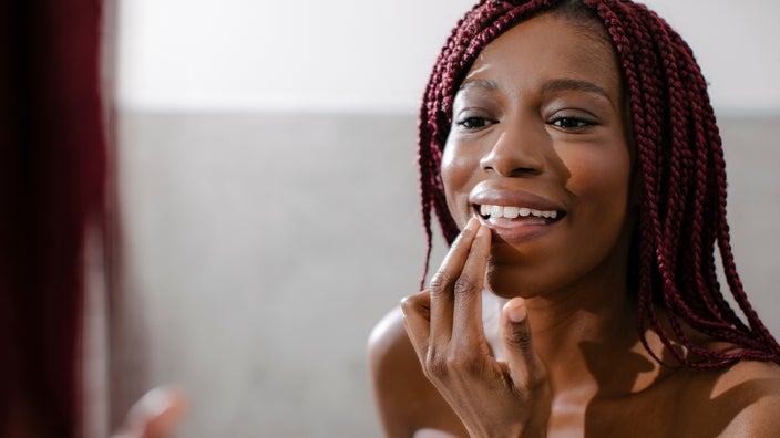 A woman applies lip balm in front of a mirror.