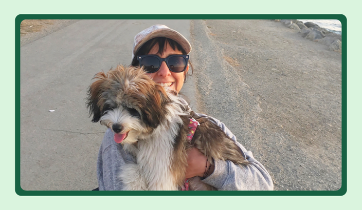 Yuri Cárdenas on a path by the water’s edge, holding a service dog named Katsu.