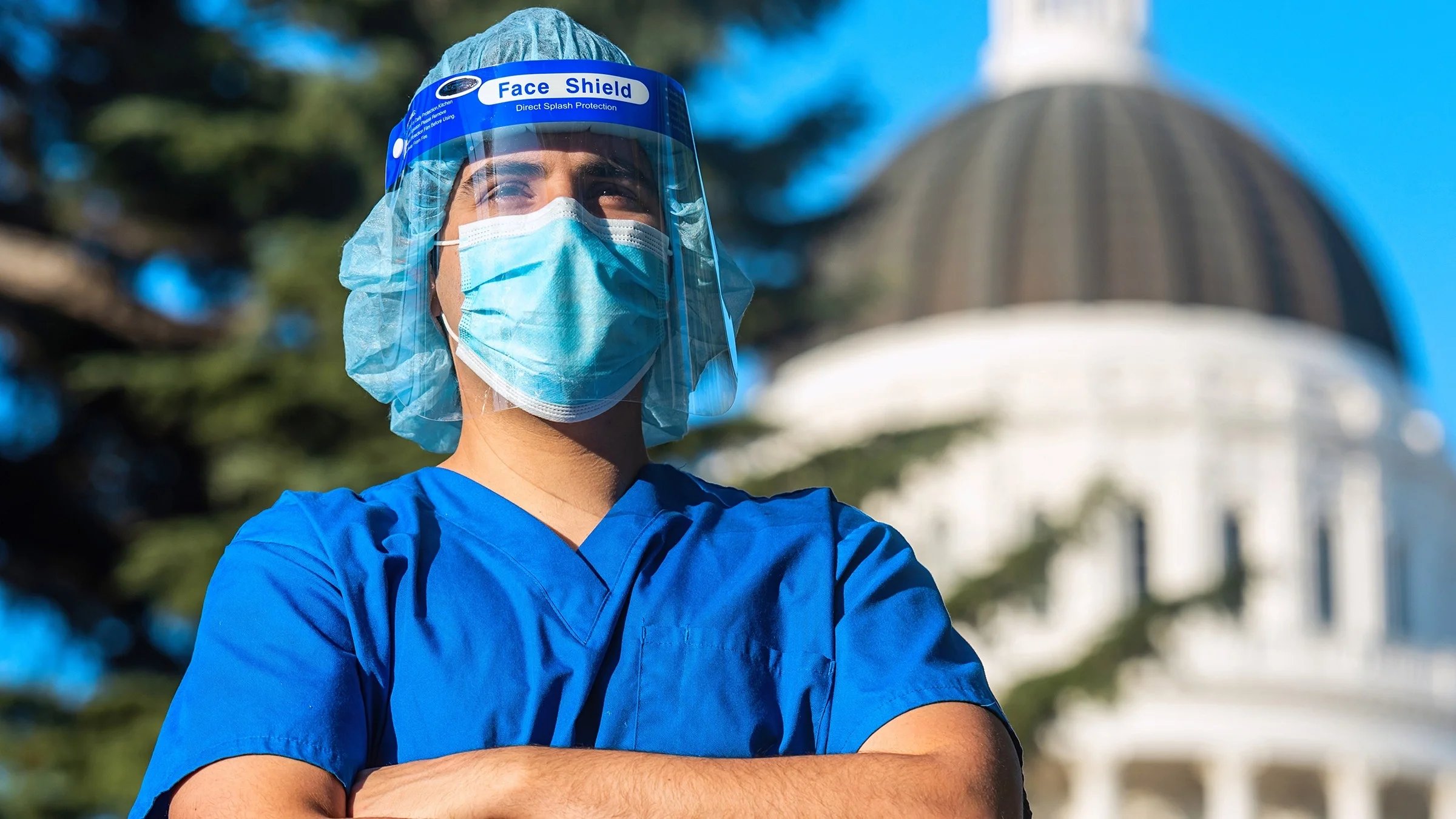 Healthcare working in scrubs and a face mask and shield standing in front of the U.S. Capitol building on a bright sunny day.