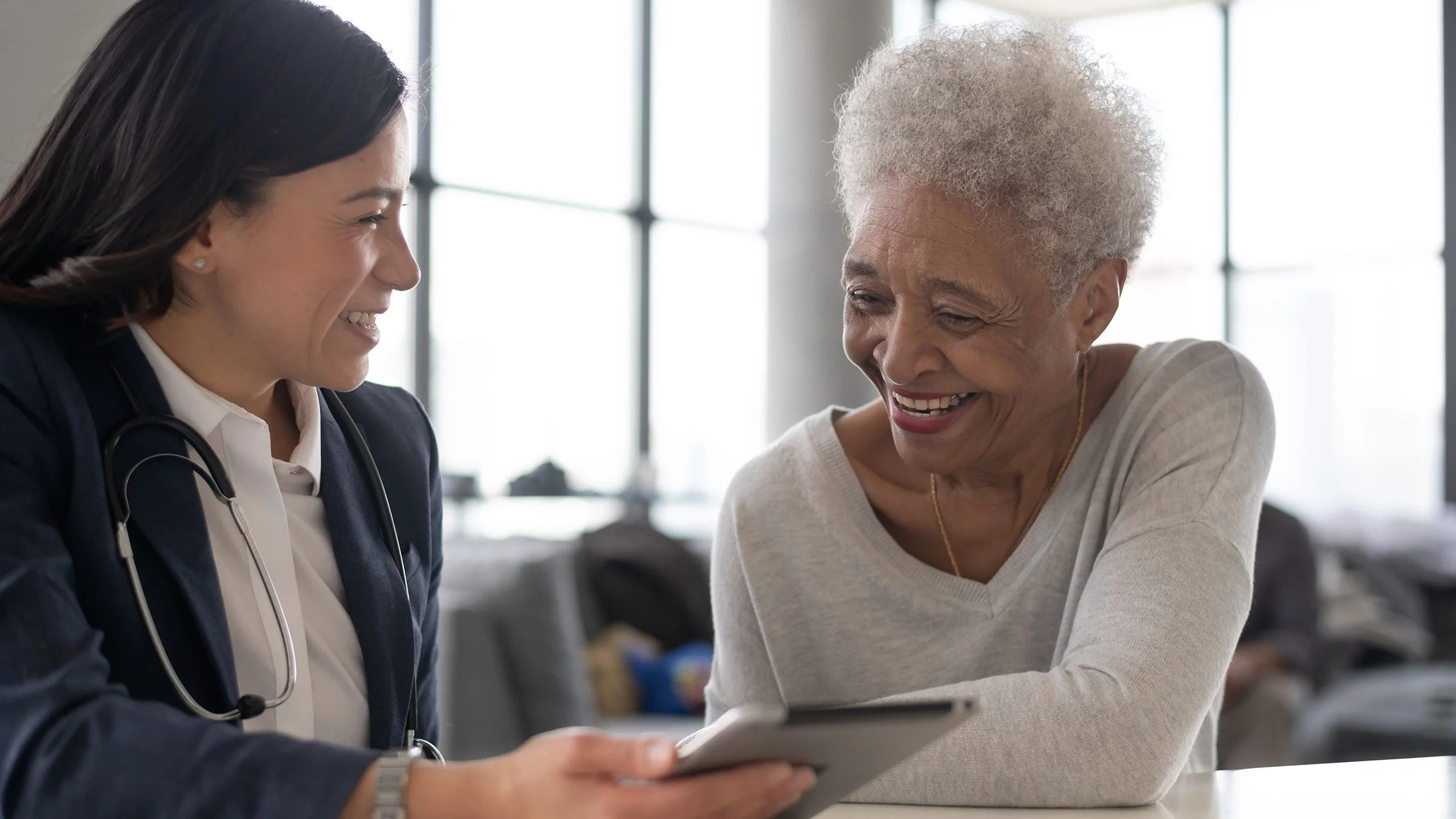 Elderly patient and doctor reviewing paperwork on a tablet device. They are both smiling.