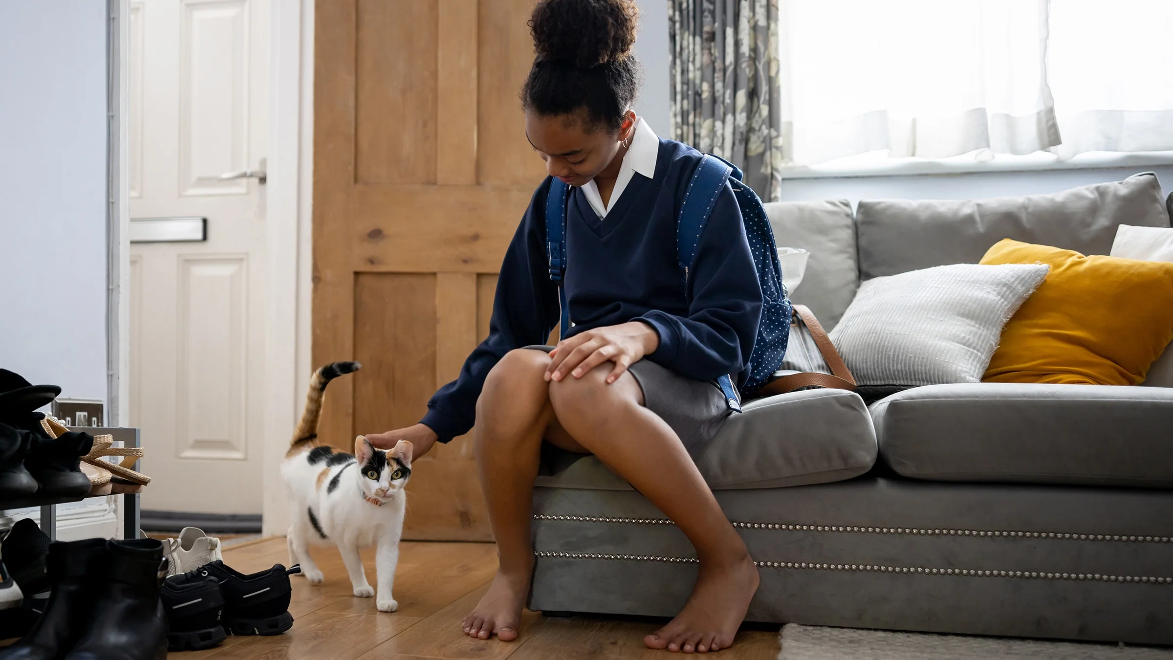 Teenage girl arriving home from school and greeting the cat.