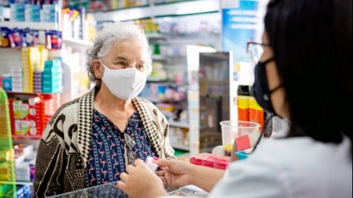 Older woman with face mask talking with pharmacist at the counter about medications.