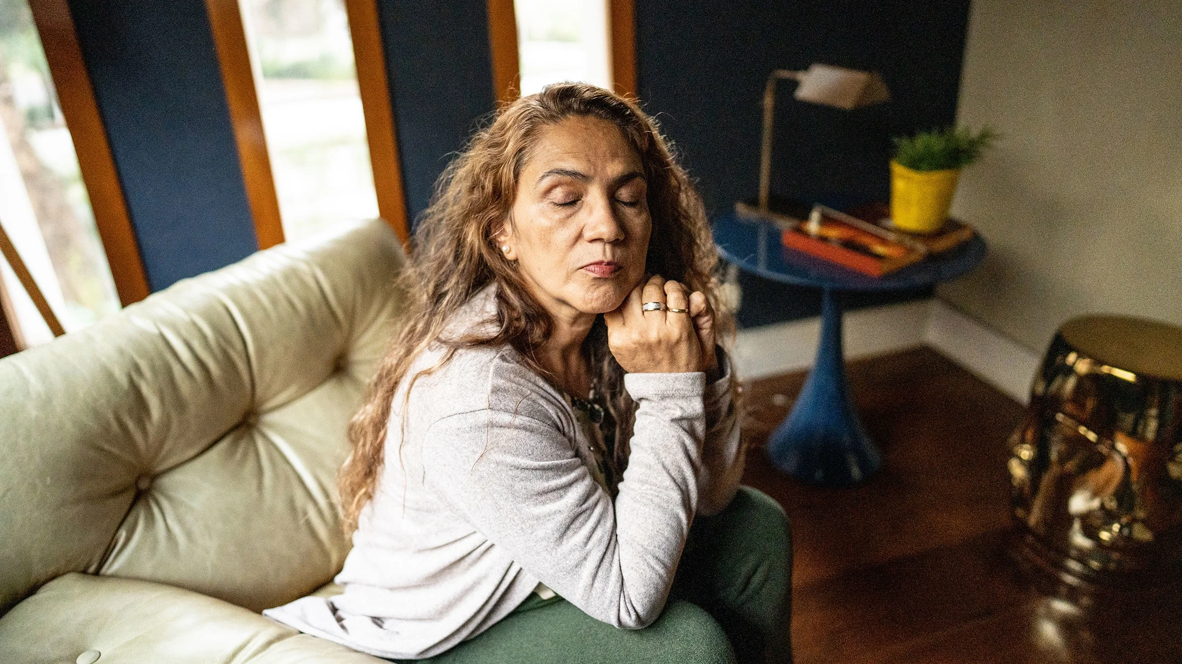 A mature woman sits on the sofa with her eyes closed.