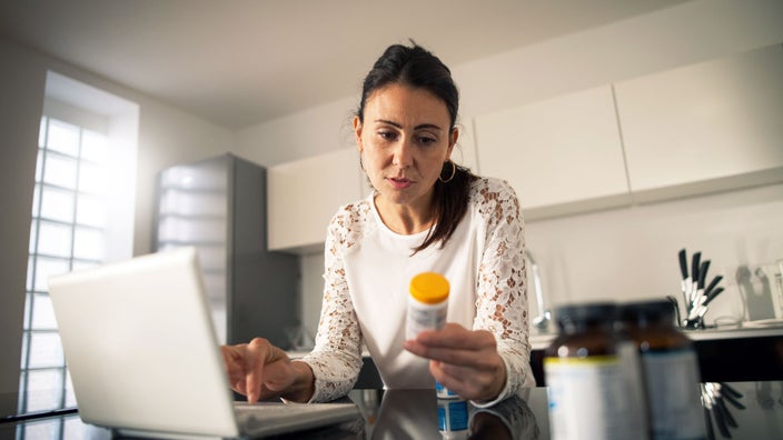 A woman is holding a prescription bottle while researching online