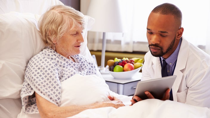 A doctor showing a tablet to a patient in a hospital bed 