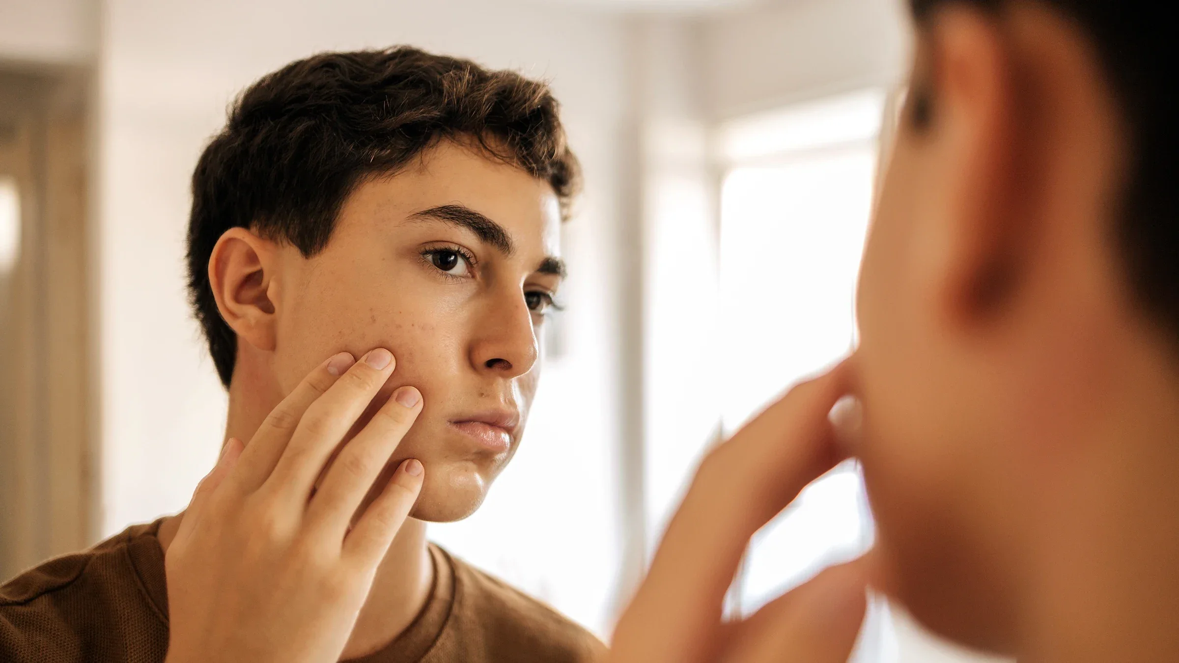 A teenager is looking at their skin in the mirror.
klebercordeiro/iStock via Getty Images Plus