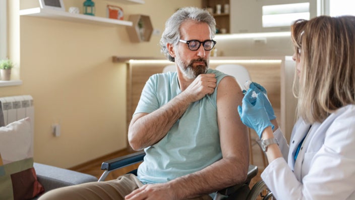Doctor cleaning a male patient's arm with a cotton swab before giving him a shot while he sits in a wheel chair.