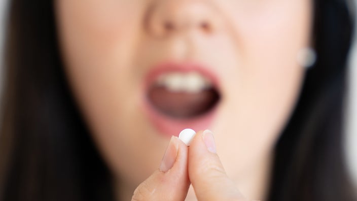 A woman prepares to take a pill by mouth.