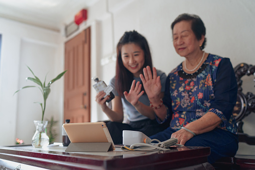 Granddaughter and grandmother at home waving hi to the doctor on a telehealth visit on their tablet.