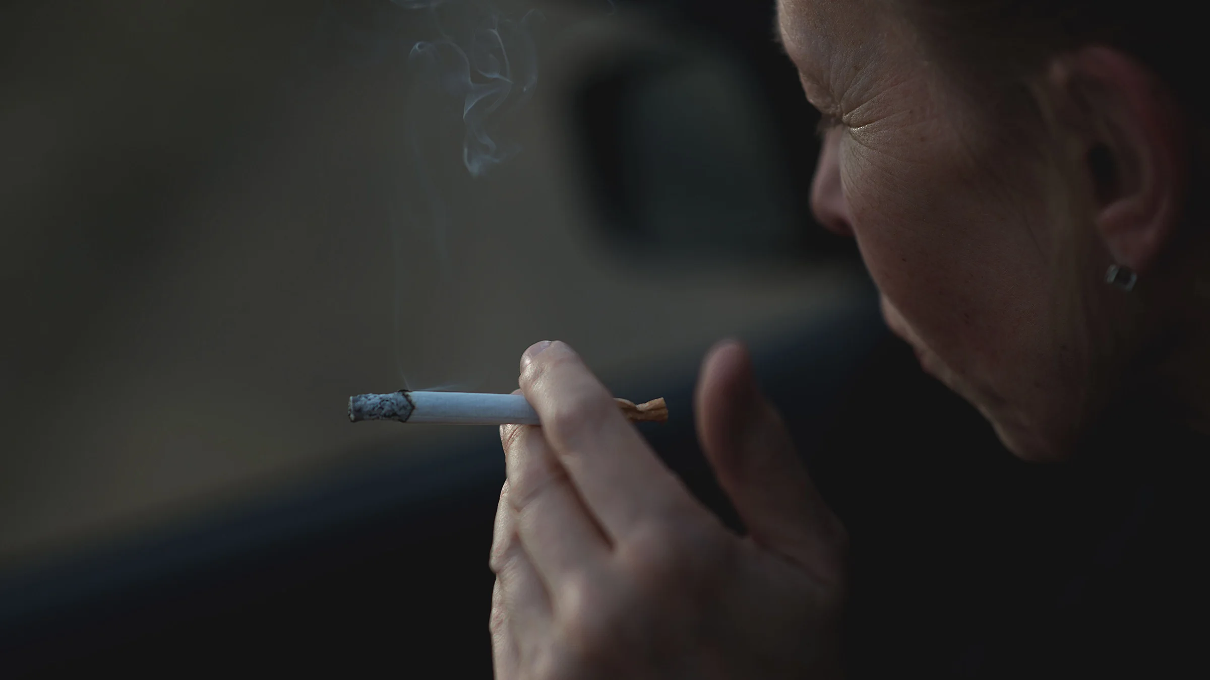 Close-up woman holding a lit cigarette in her hand.