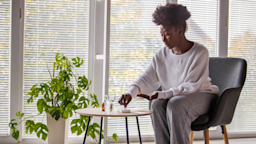 A woman sits down and takes pills out of a pill planner box. 
fotostorm/E+ via Getty Images Plus