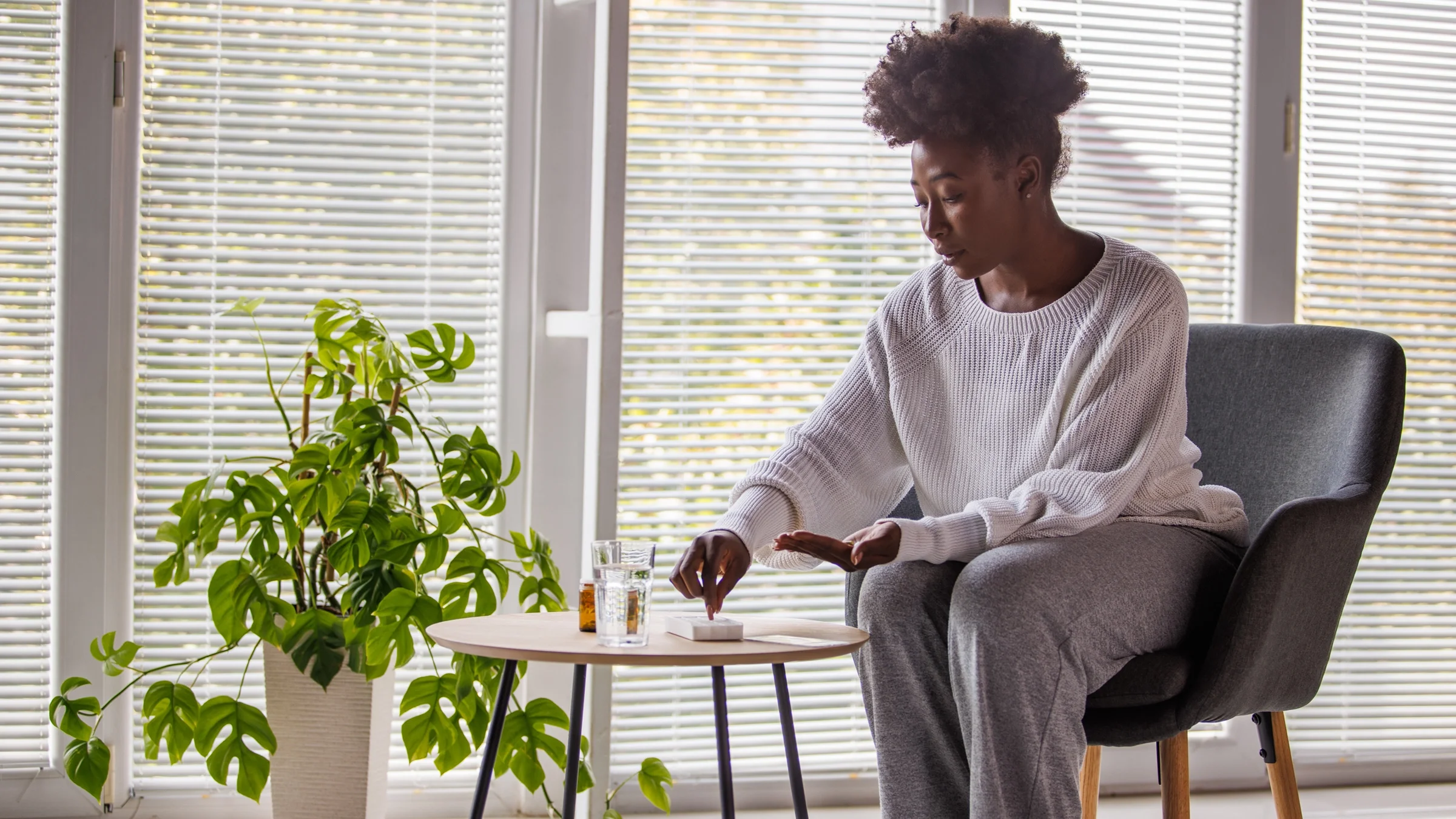 A woman sits down and takes pills out of a pill planner box. 