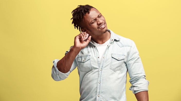 Portrait of a man rubbing his ear on a yellow background.