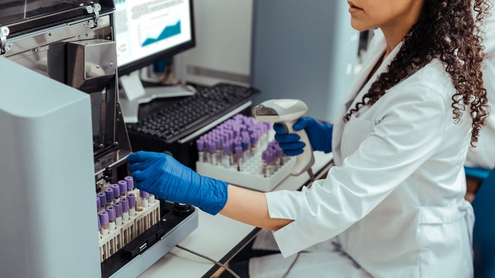 Medical worker uses scanning gun to mark the blood samples for testing in the lab while sitting down.