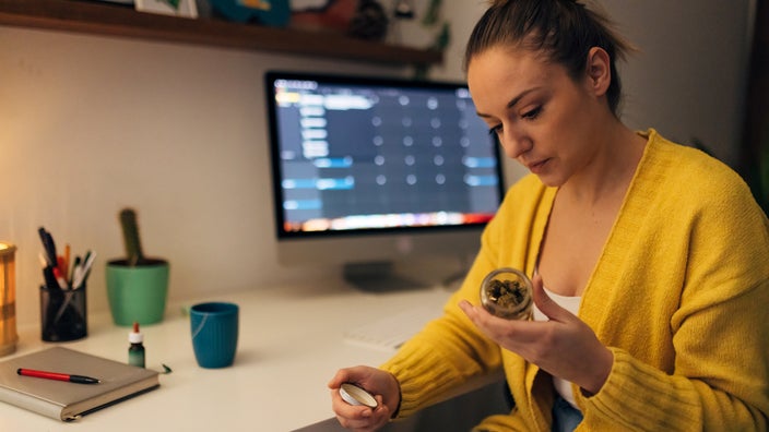 Woman reads a glass bottle containing cannabis buds.