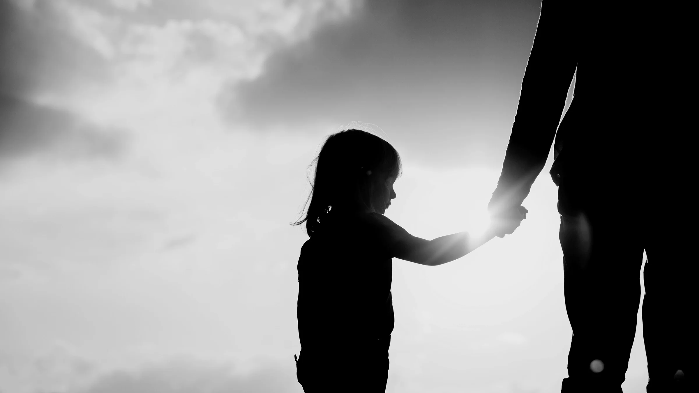 Black-and-white image of a young girl's silhouette holding her parent's hand.