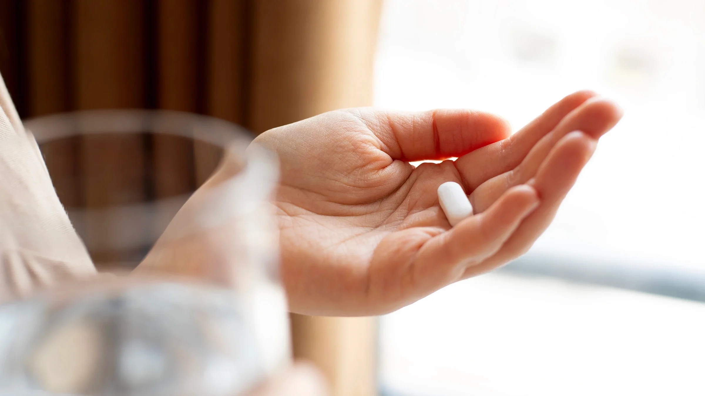 The image shows a close-up of a person preparing to take a pill with a glass of water.