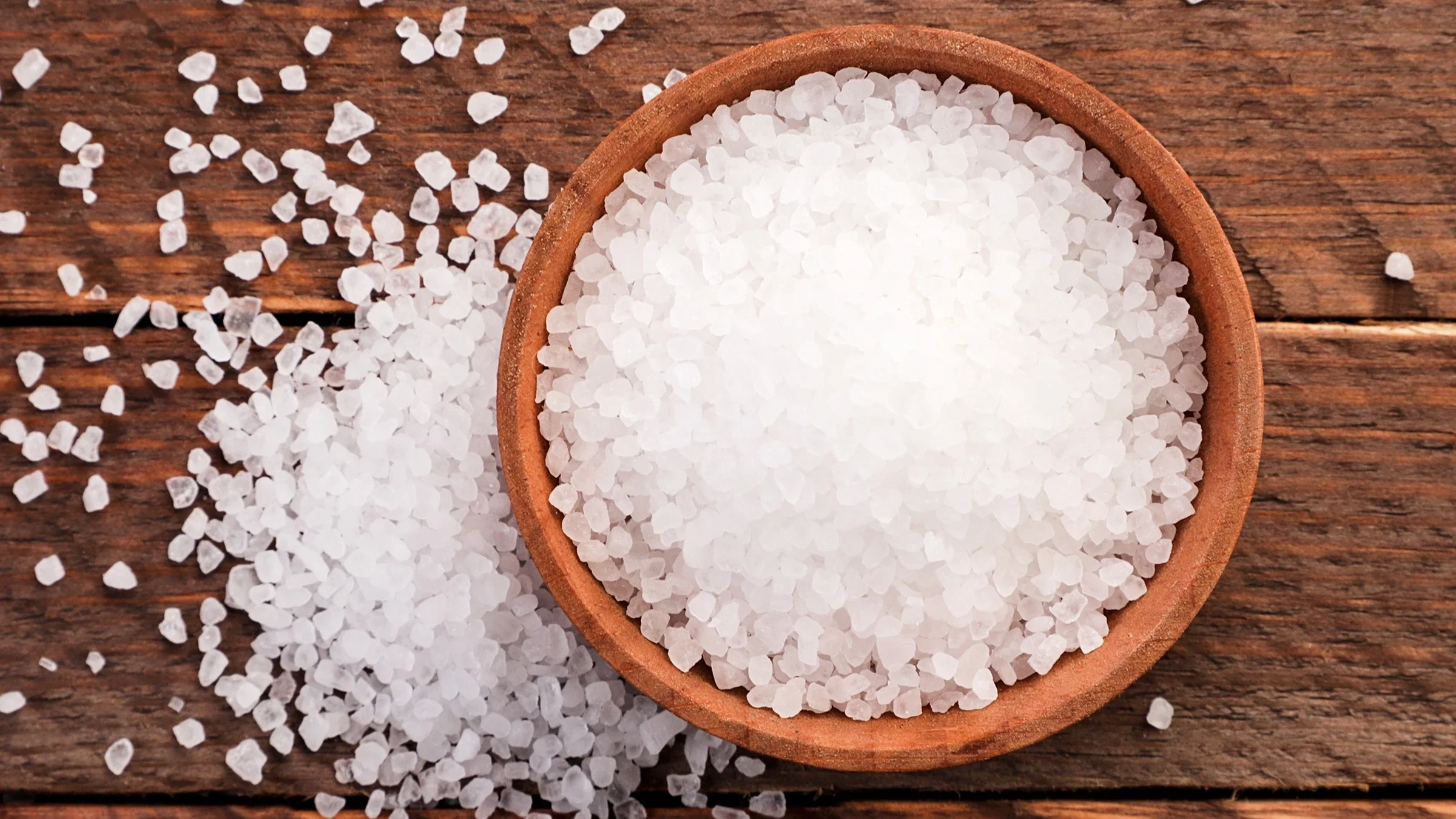 Close-up of a wooden bowl of coarse salt with it spilling over on to the table.
