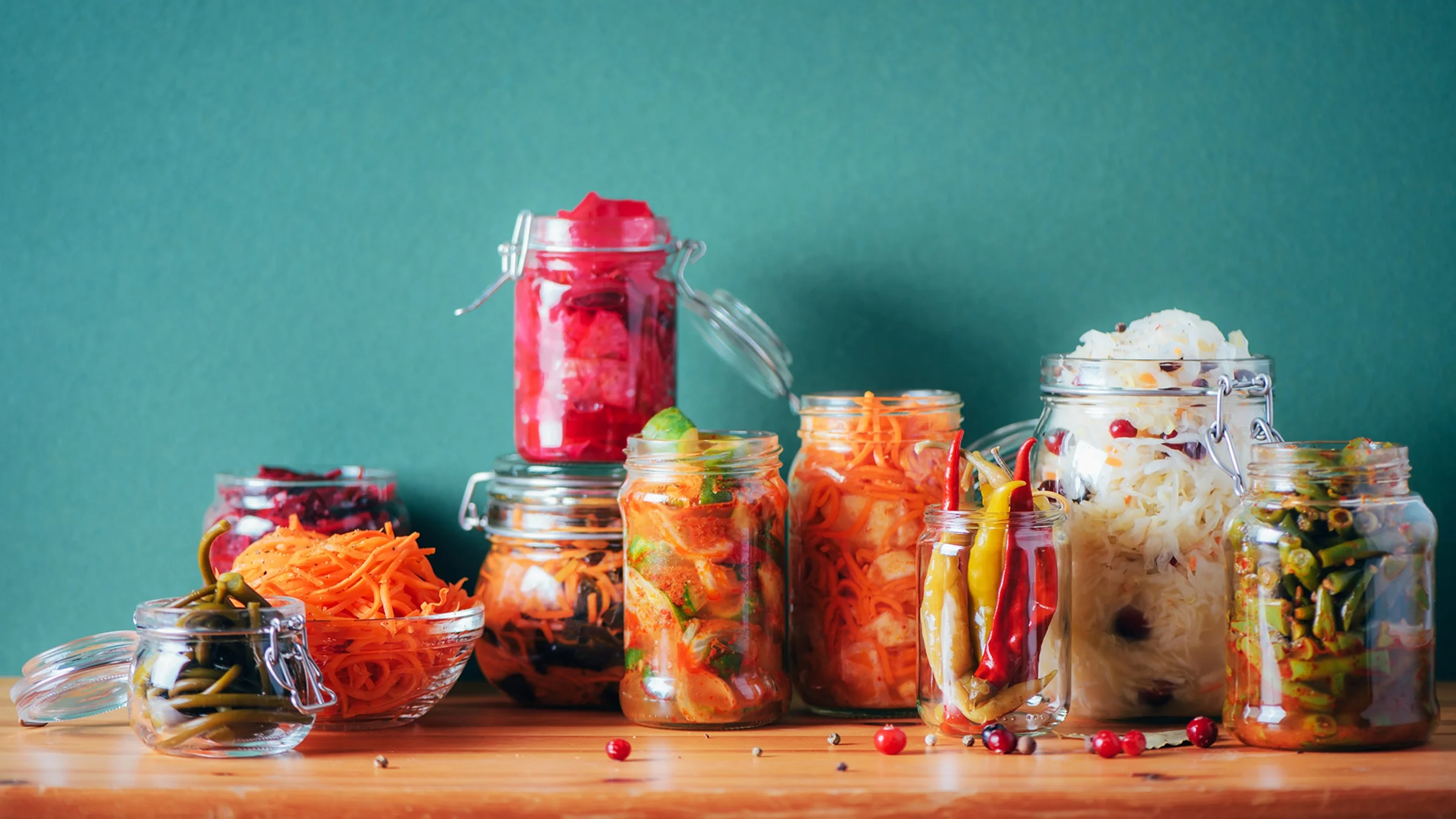 Jars of fermented food on a wooden countertop against a teal wall.