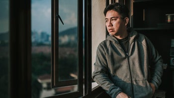 Health: Mental health: younger man staring out window-1219351014