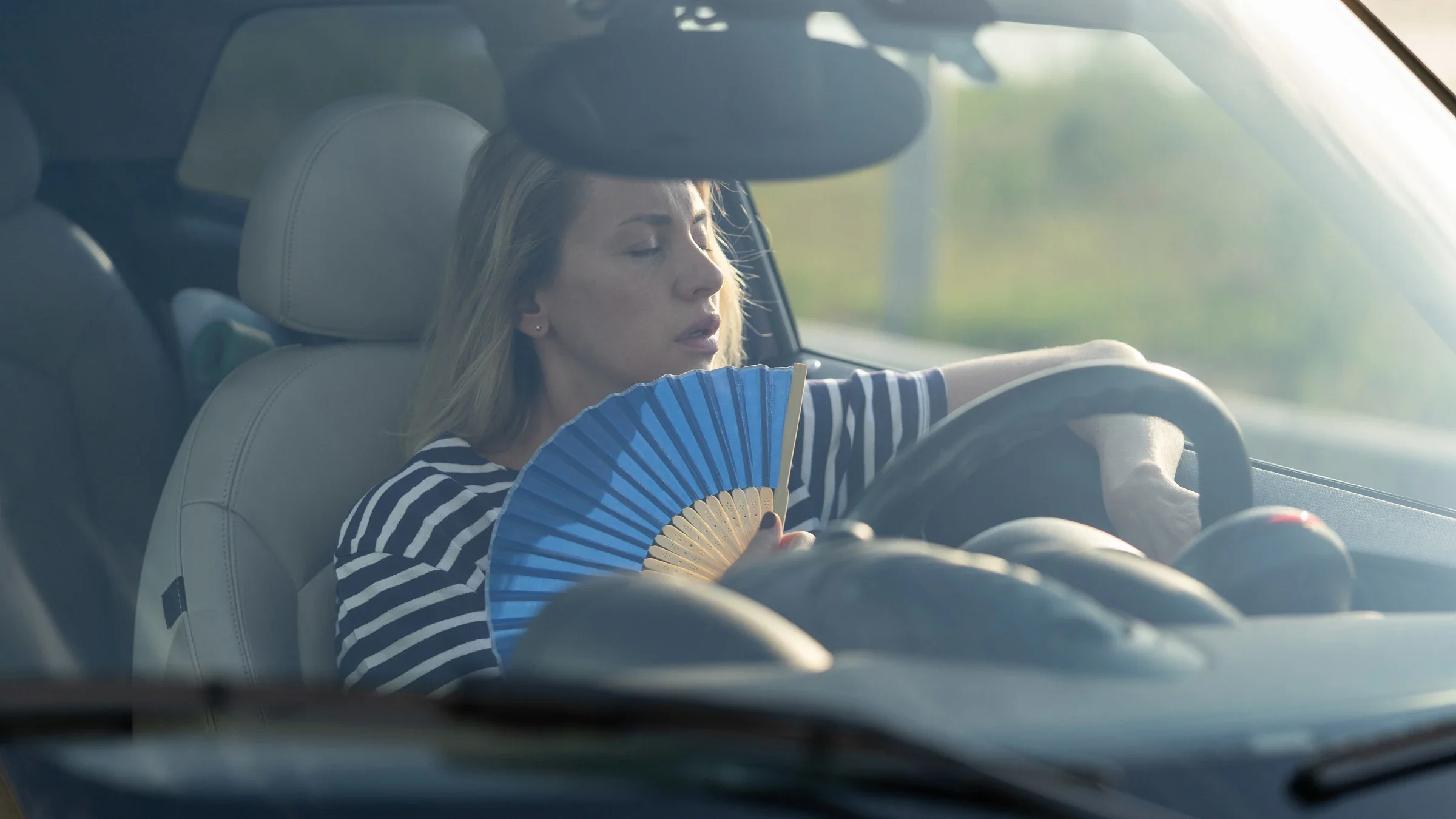 A person using a hand fan in their car on a hot summer day.
Dima Berlin/iStock via Getty Images 