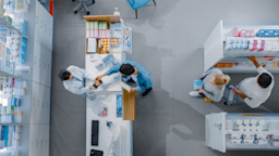 Overhead view of pharmacy checkout counter. A pharmacist is helping out a customer at the counter, while two other people wait in line.
gorodenkoff/iStock via Getty Images Plus