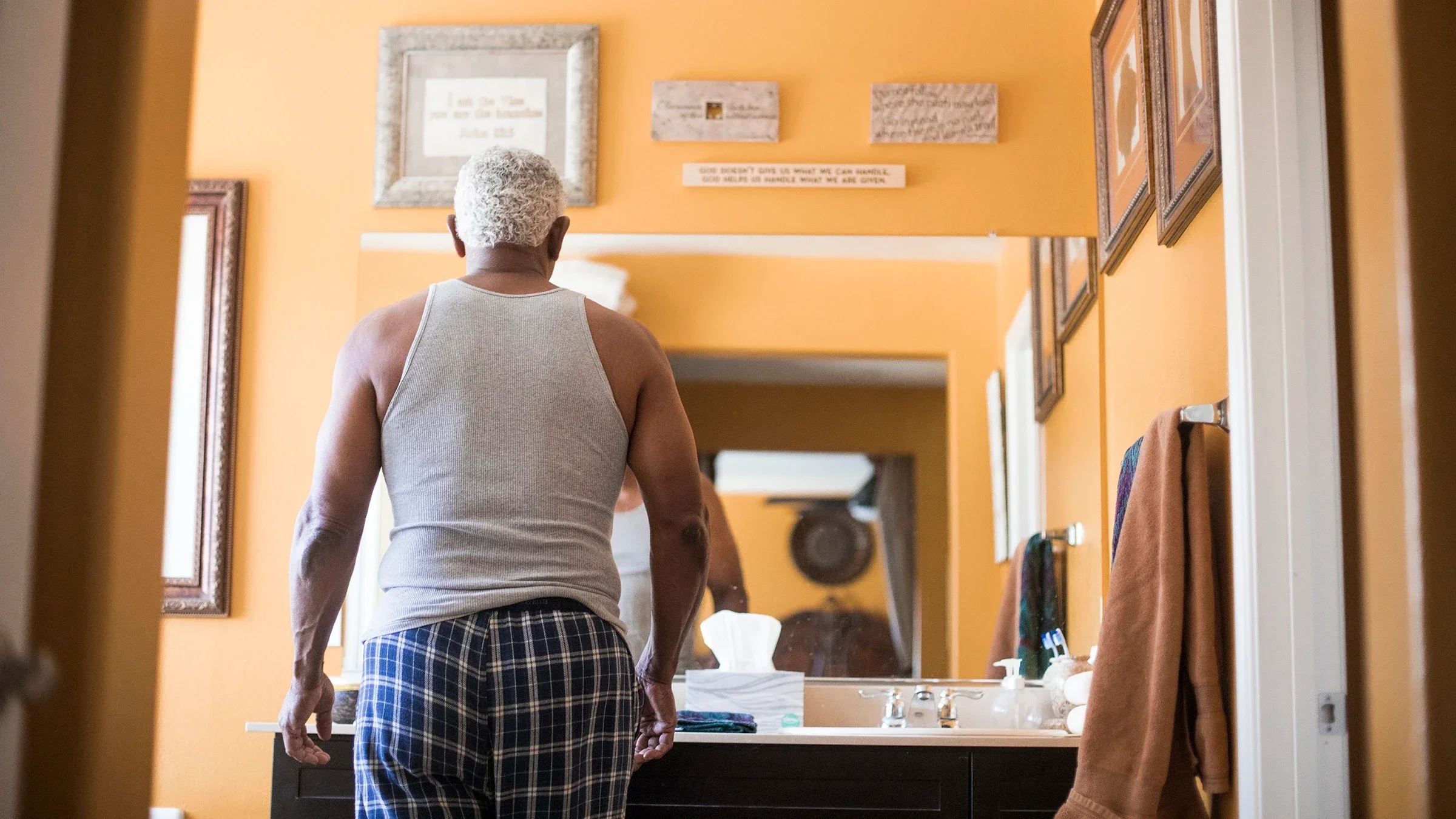Senior man getting ready in the bathroom mirror. We are looking at his back through the doorway.
adamkaz/E+ via Getty Images
